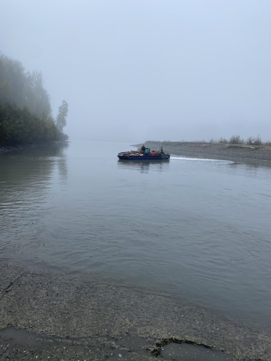 A boat disappearing into thick fog on a wide gray river