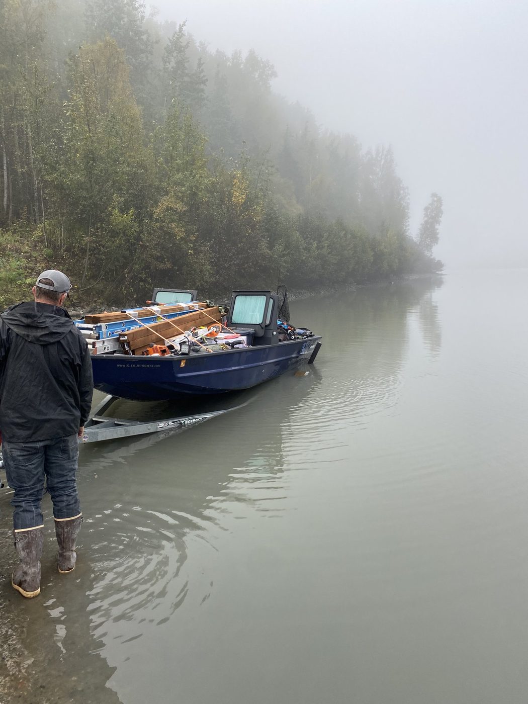 A small boat overloaded with lumber, ladders, a chainsaw and fuel at a riverbank