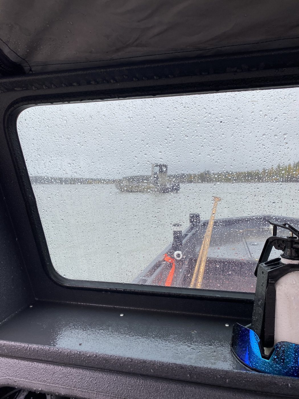 Rain-streaked view through a boat cabin window on a gray river