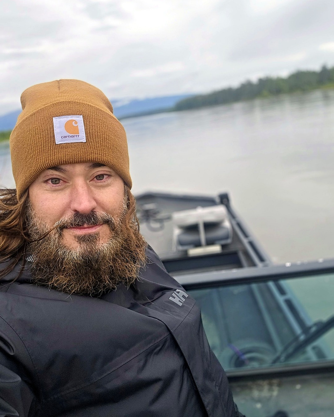 Chad in a Carhartt beanie on the boat, river behind, heading out to the property