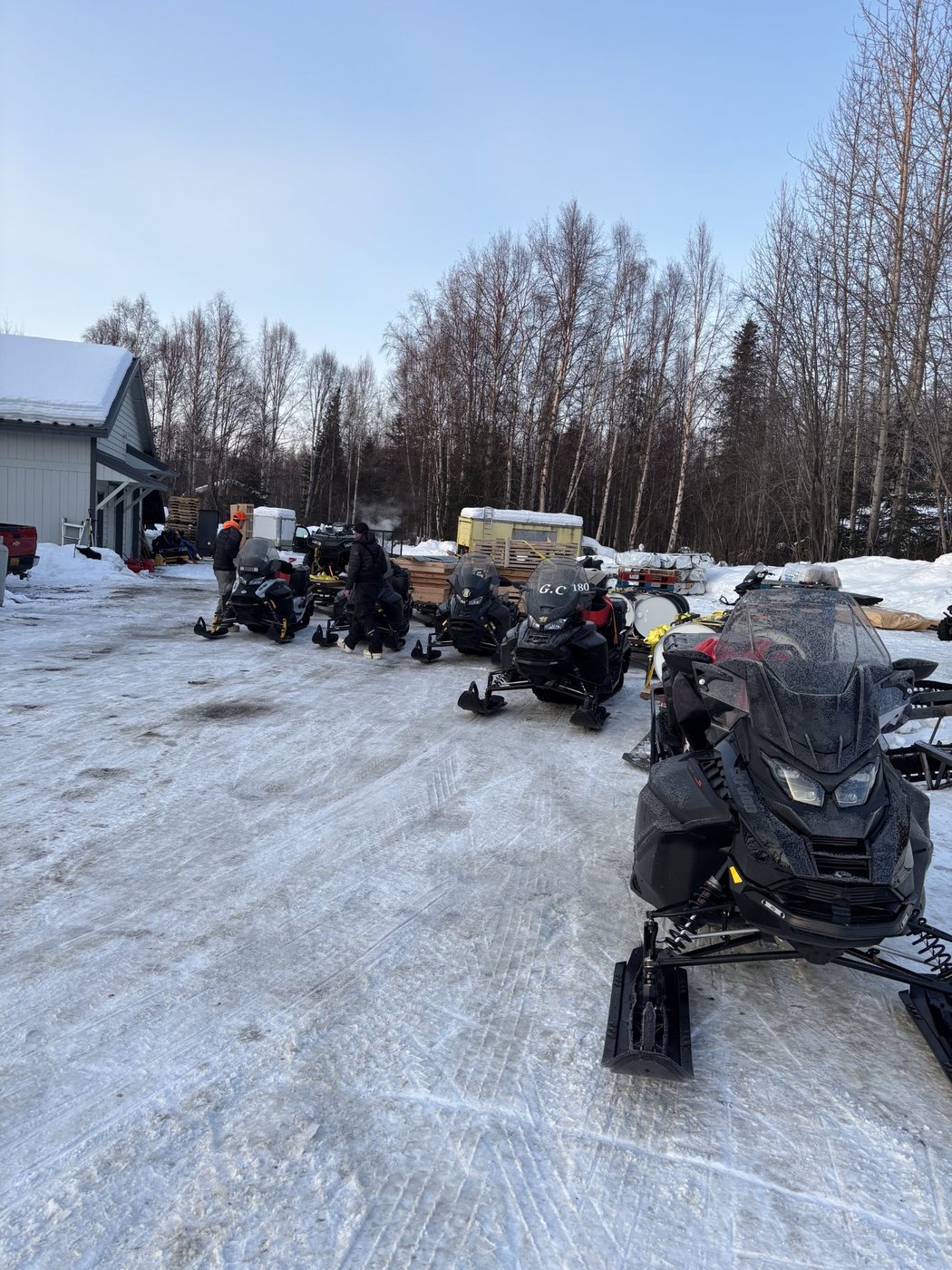 Snow machines parked by a building with crew members preparing for a freight run
