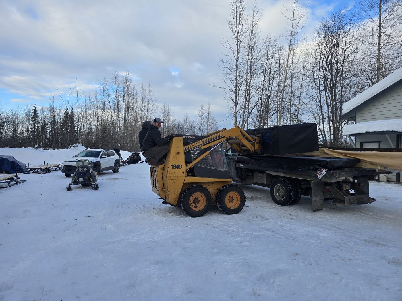 Chad riding on the back of the Case skid steer as it loads a flatbed truck