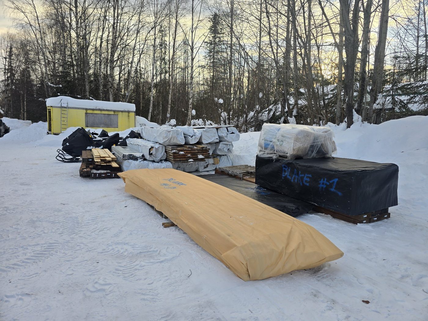 Wrapped lumber bundles staged in the snow, one marked Blake #1